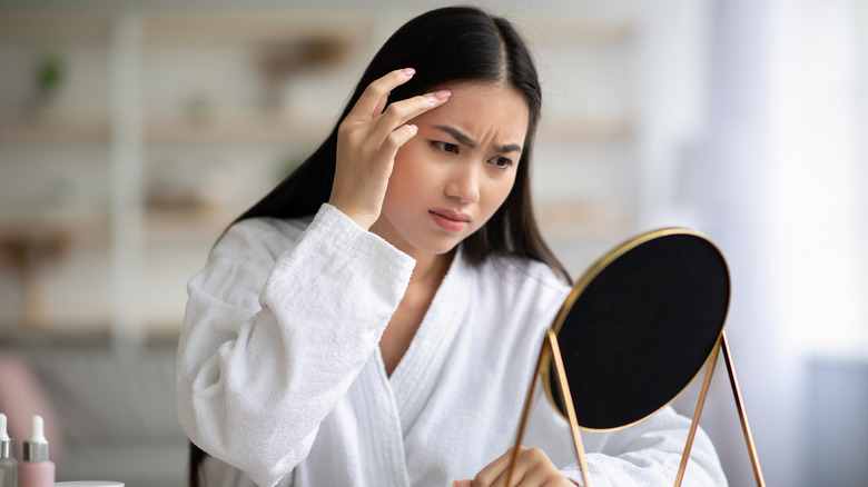 A woman looking disapprovingly at her forehead in the mirror