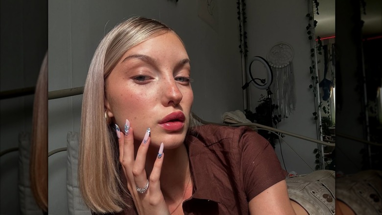 A woman wearing a brown shirt and posing to model her makeup