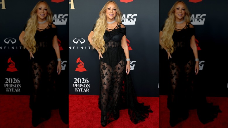 Mariah Carey on the 2026 MusiCares Person of the Year red carpet. She is wearing a long black gown that is sheer, with floral appliques and a black bustier.