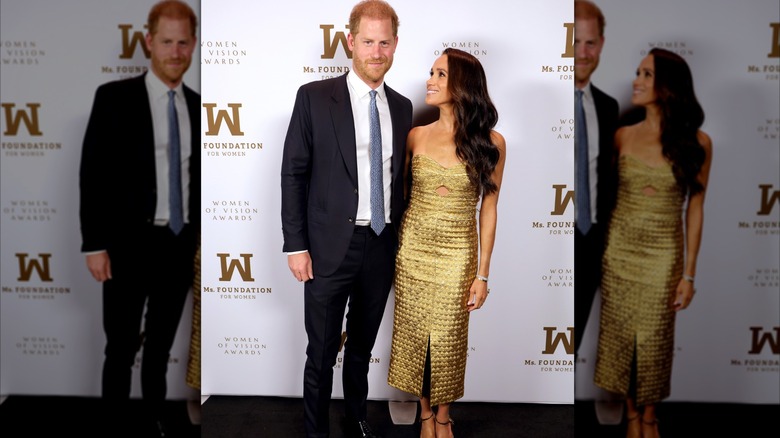 Meghan Markle wearing a gold dress poses beside Prince Harry at the  the Ms. Foundation Women of Vision Awards red carpet