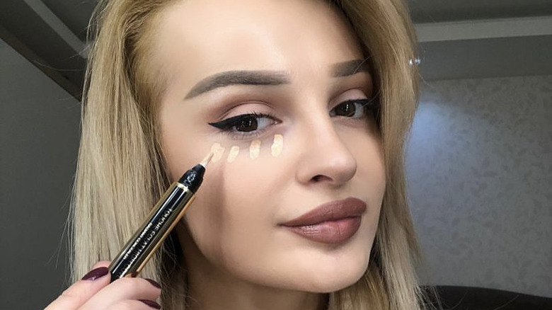 person applying YSL concealer to undereye