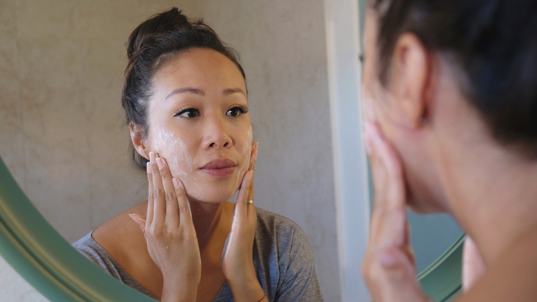 woman exfoliating face in mirror