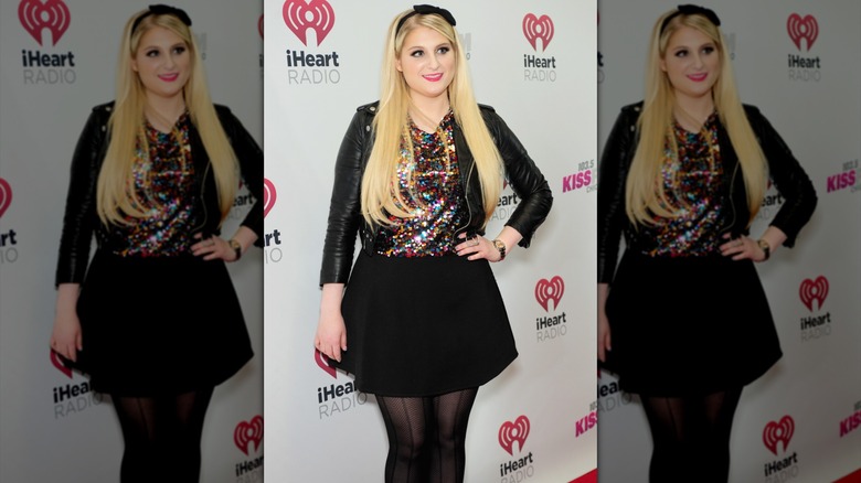 Meghan Trainor posing on the red carpet wearing a black headband and sequined top