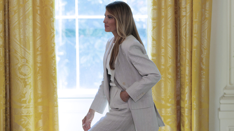 Melania Trump walking with one hand in her pocker while wearing a Max Mara pinstriped suit