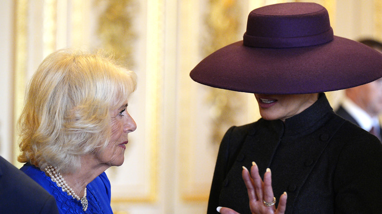 Melania Trump wearing a purple wide-brimmed hat while speaking with Queen Camilla