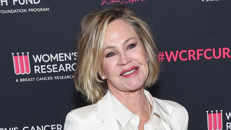 Melanie Griffith poses with her head tilted in a white shirt at a charitable event.