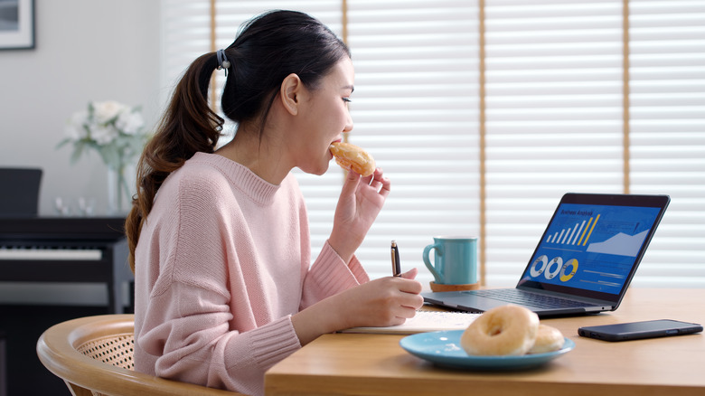 woman eating doughnut at desk