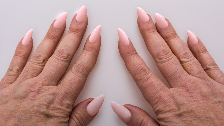Middle-aged hands with light-pink stiletto nails.