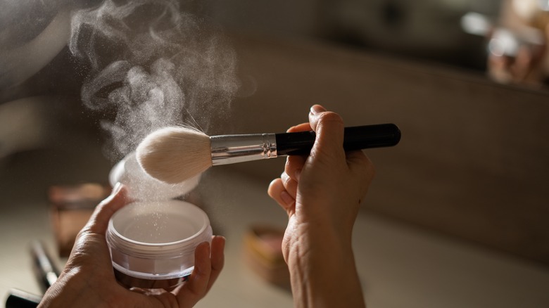 Makeup brush tapping off cloud of powder