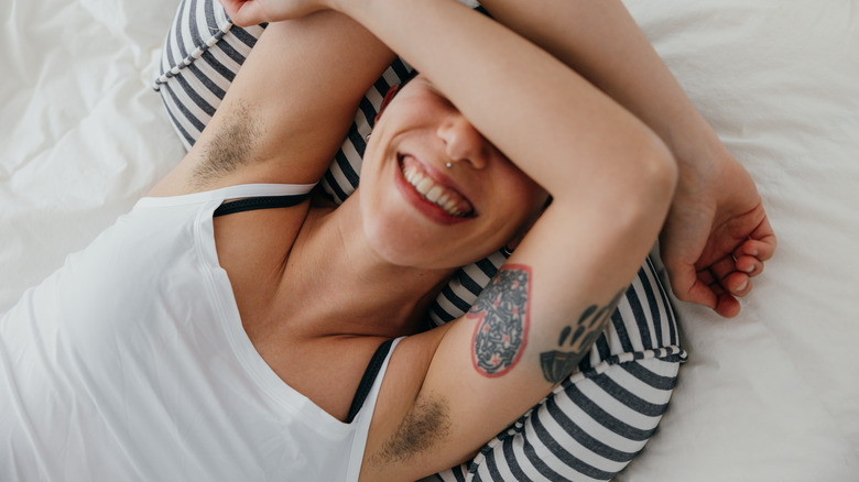A woman with tattoos lying on the bed showing her armpit hair