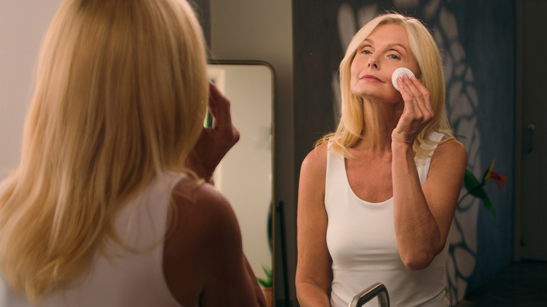 Woman in a white tank top powdering her face