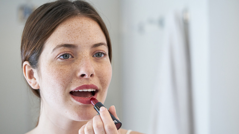 Woman with blue eyes applying red lipstick