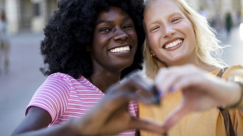 Two women smile, making a heart with their hands