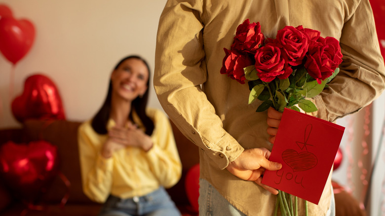 A man holds roses and a card behind his back