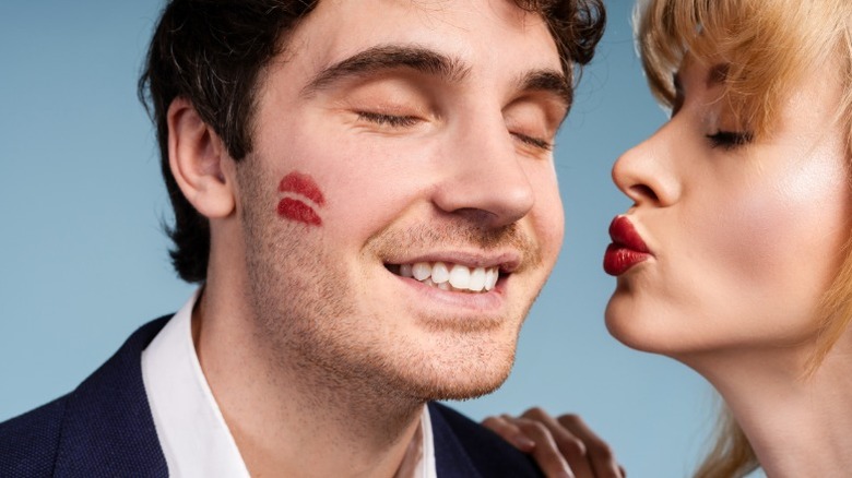 A man with a red lip kiss on his cheek and a woman puckered up next to him