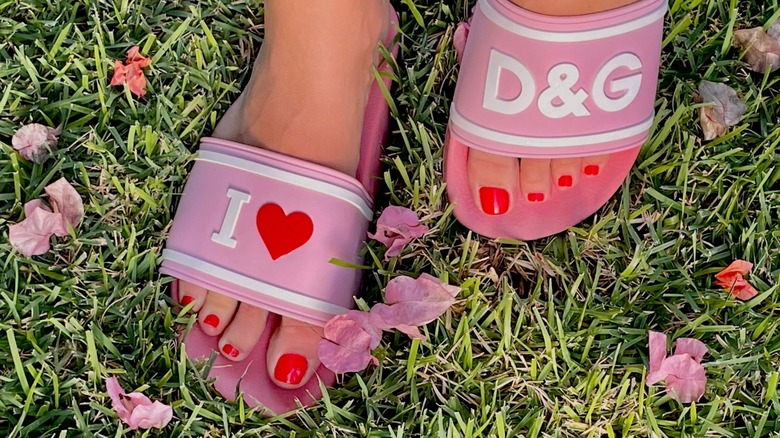 A woman's feet with bright red toenails in Dolce & Gabbana sandals.