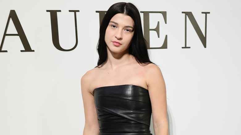 Phoebe Gates in black leather strapless dress with her hair down and parted in the middle