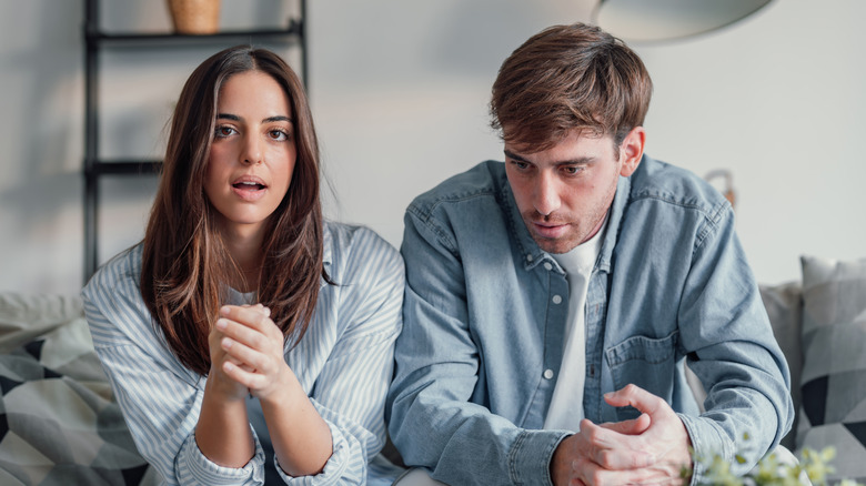 A young couple sitting on a couch arguing.