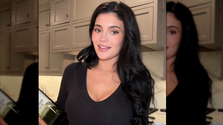 Kylie Jenner with a no-makeup makeup look holding a bottle of Smash Oil