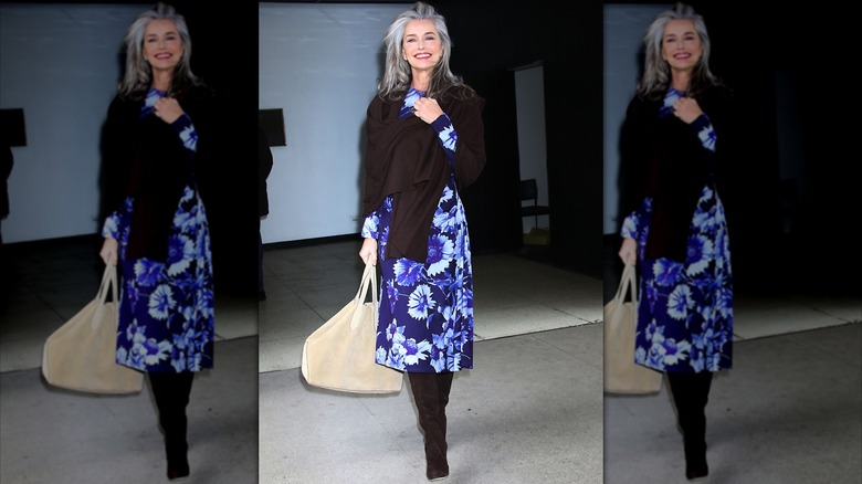 Paulina Porizkova walking in a blue floral dress and black sweater and boots.
