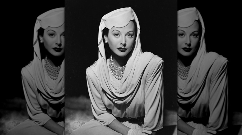 Hedy Lamarr wears a pillbox hat, pearls, and a head scarf