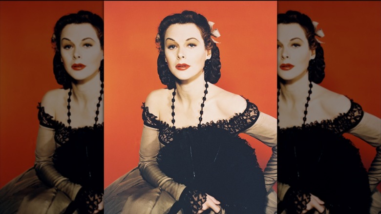 Hedy Lamarr wearing a beige dress with black lace and holding a fan