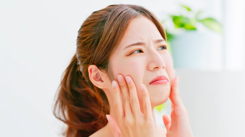 frowning young Asian woman touching face