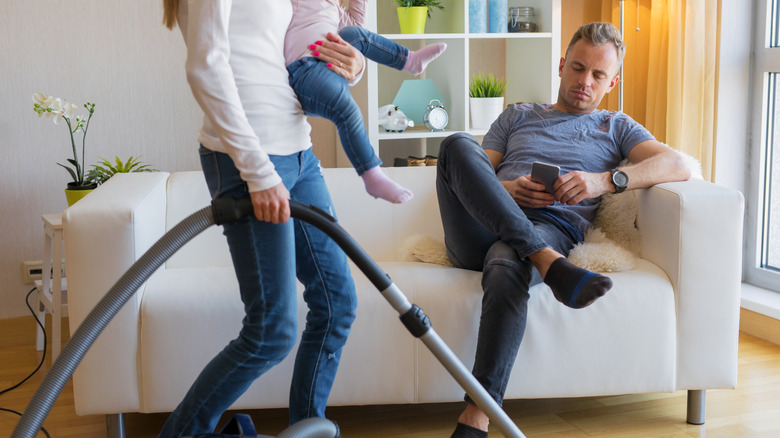 Woman doing chores while man lounges