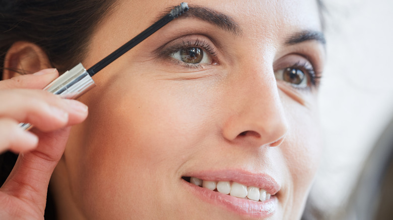 Woman fixing eyebrow in mirror