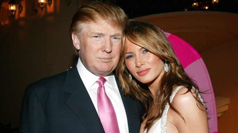 Melania Trump wearing a white dress leaning into Donald Trump who is wearing a black suit
