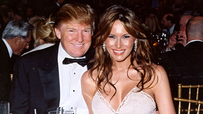Donald Trump wearing a black suit and Melania Trump wearing a white dress while posing for a photo at a New Year's party in Mar-a-Lago