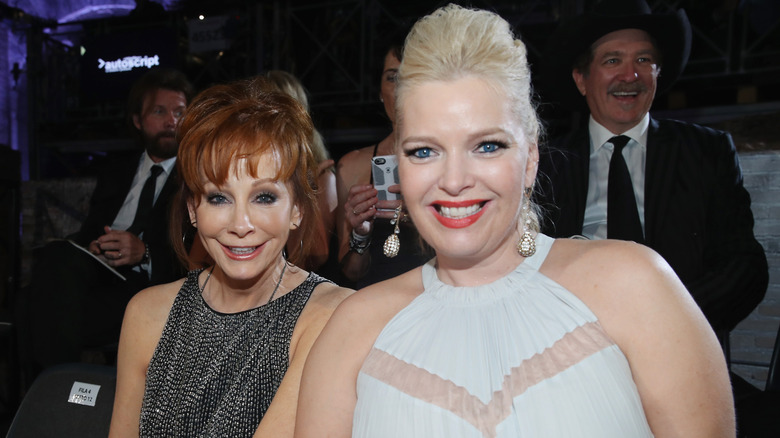 Reba McEntire wearing a sparkly black dress and Melissa Peterman wearing a white dress sitting together.