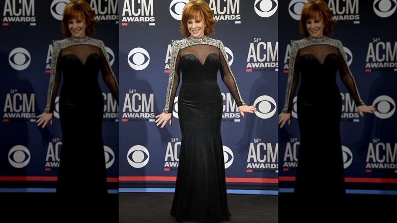 Reba McEntire in the 2019 ACM Awards press room red carpet in a tight dress with detail on the shoulders..
