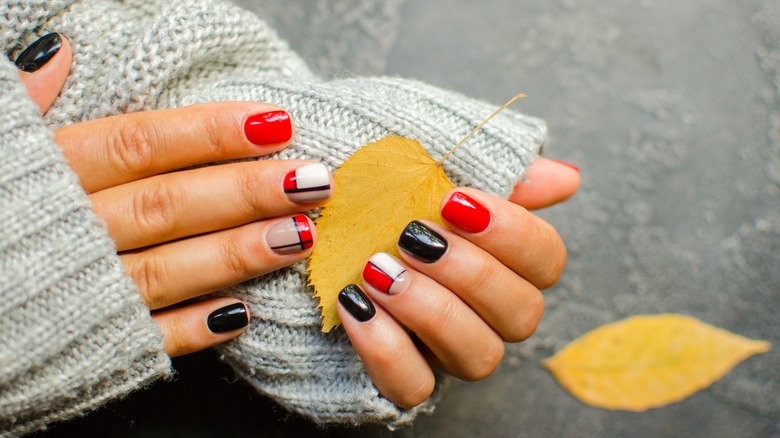 Hands with red and black nail art holding yellow leaf