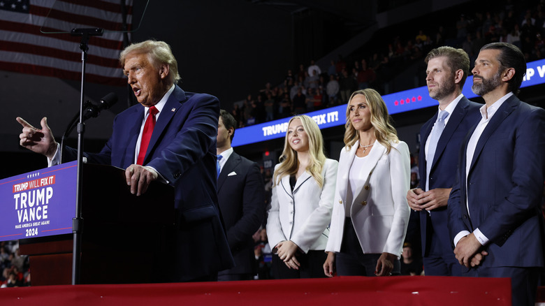Lara and Eric Trump stand behind Donald Trump while he gives a speech.