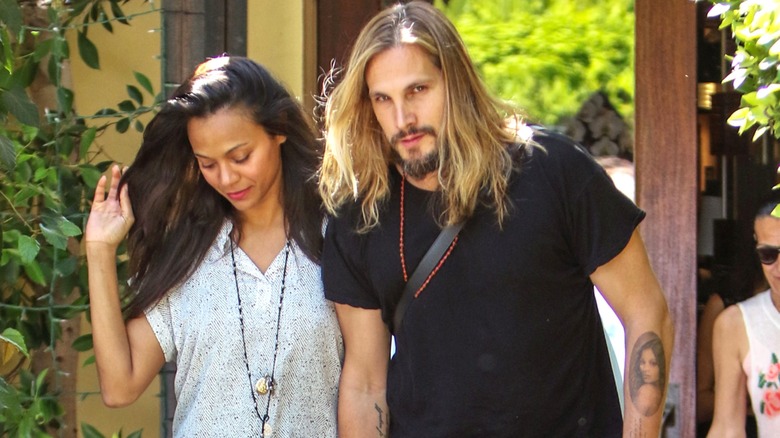 Zoe Saldaña and Marco Perego-Saldaña walking together, with his tattoo of Zoe visible.