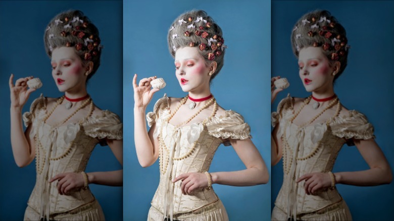 woman in Victorian style makeup and corset dress styled with pearls staring at a pastry