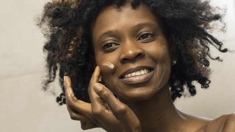 Woman applying cream to face in bathroom mirror