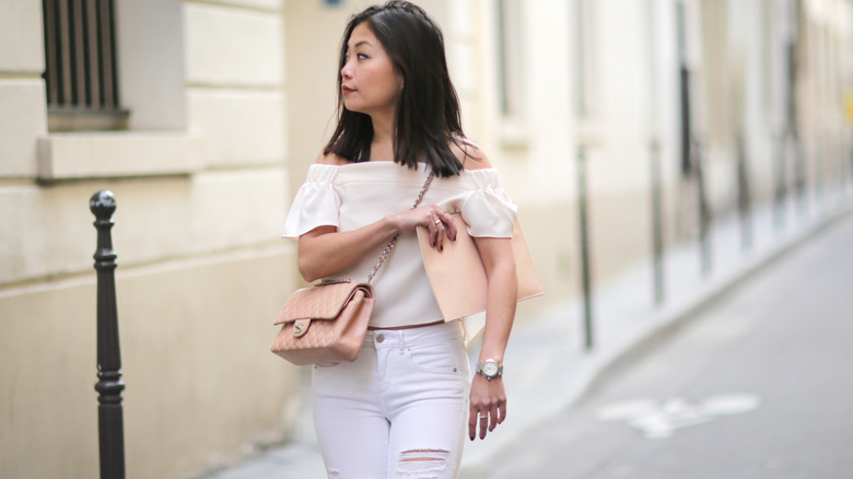 A woman wearing ripped white jeans and an off-the-shoulder top