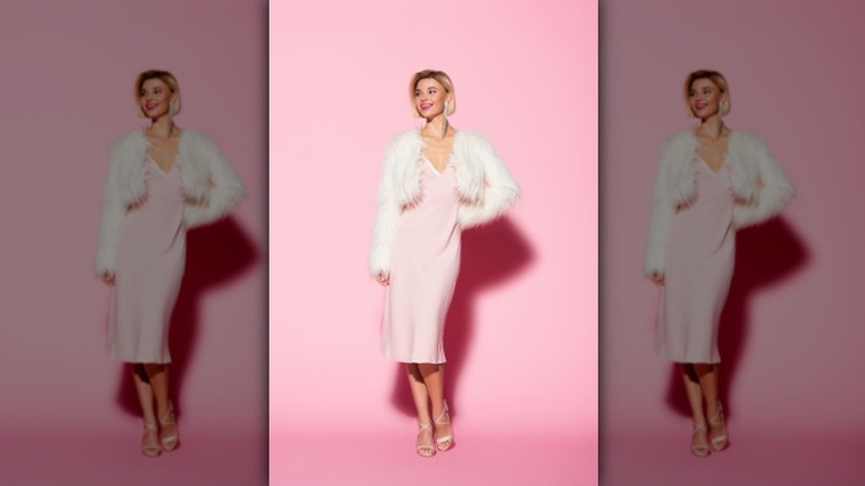 woman wearing baby pink slip dress with a white fluffy jacket