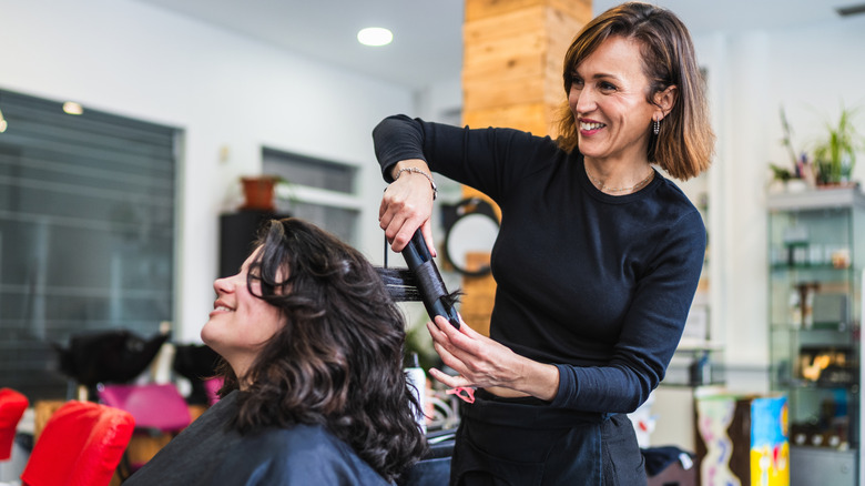 A hairstylist smiling while using a hair tool on a client