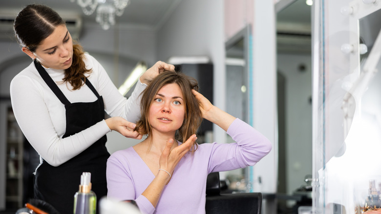 A woman giving direction to her hair stylist at the salon.