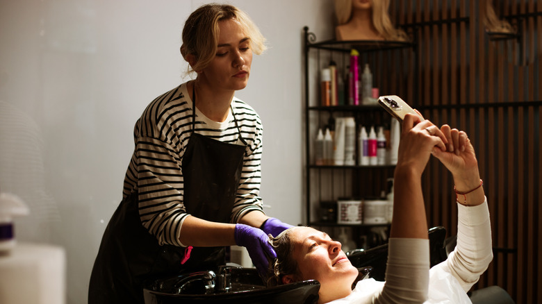 Client taking a selfie while the stylist is trying to wash their hair