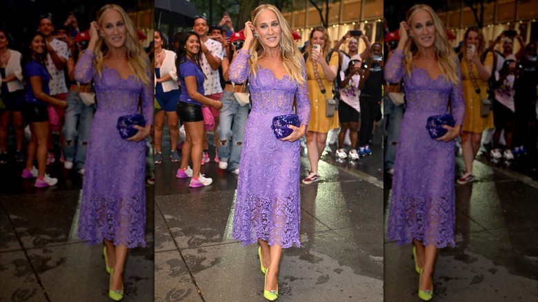 Sarah Jessica Parker posing at an event in 2023 with her hand by her head wearing a purple lace dress.