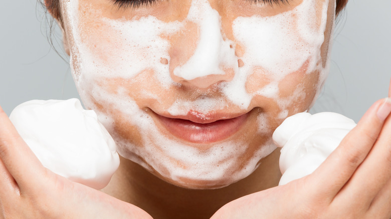 female washing her face frothy white lather in her hand