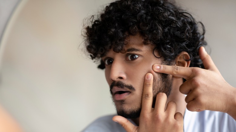 Man popping pimple in mirror