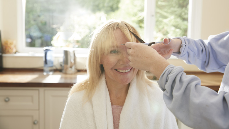 A woman with blond hair getting her bangs cut