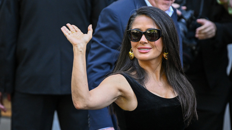 Salma Hayek waving with her grays showing and sunglasses