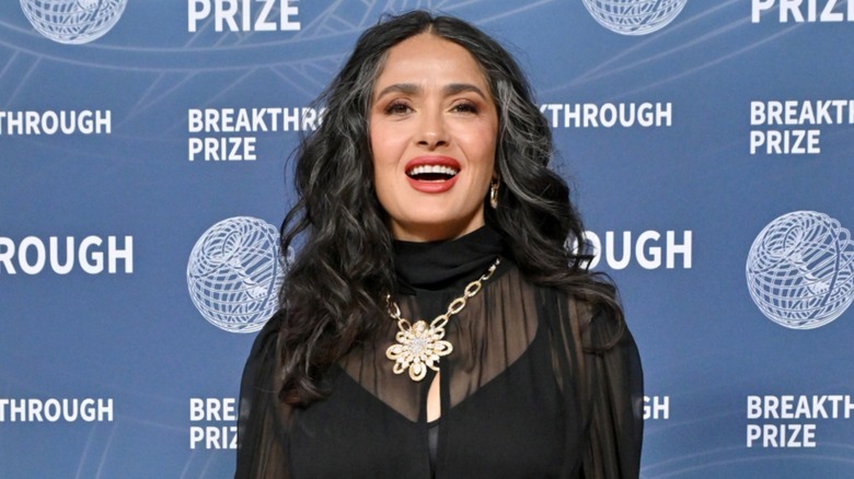 Salma Hayek posing in a sheer black top with her grays showing