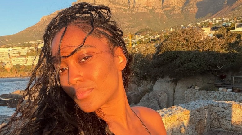 Ciara Miller posing in front of the ocean with braids and a makeup-free look
